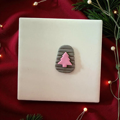 Gray clay arch with pink tree imprint centered on white tile with red fabric and pine branches