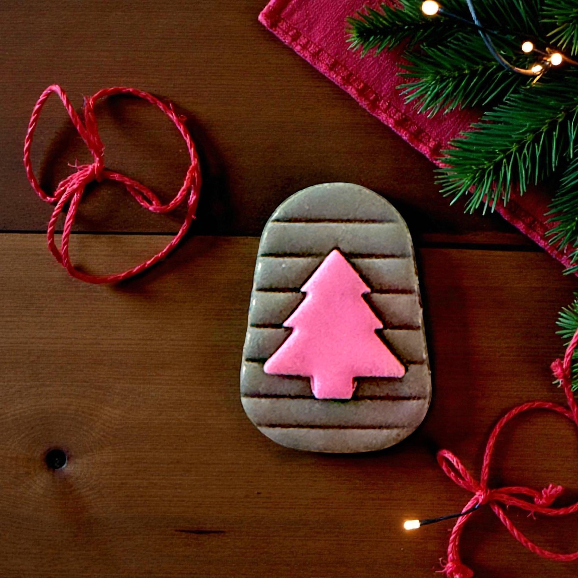 Gray clay arch with pink tree imprint centered on white tile with red fabric and pine branches