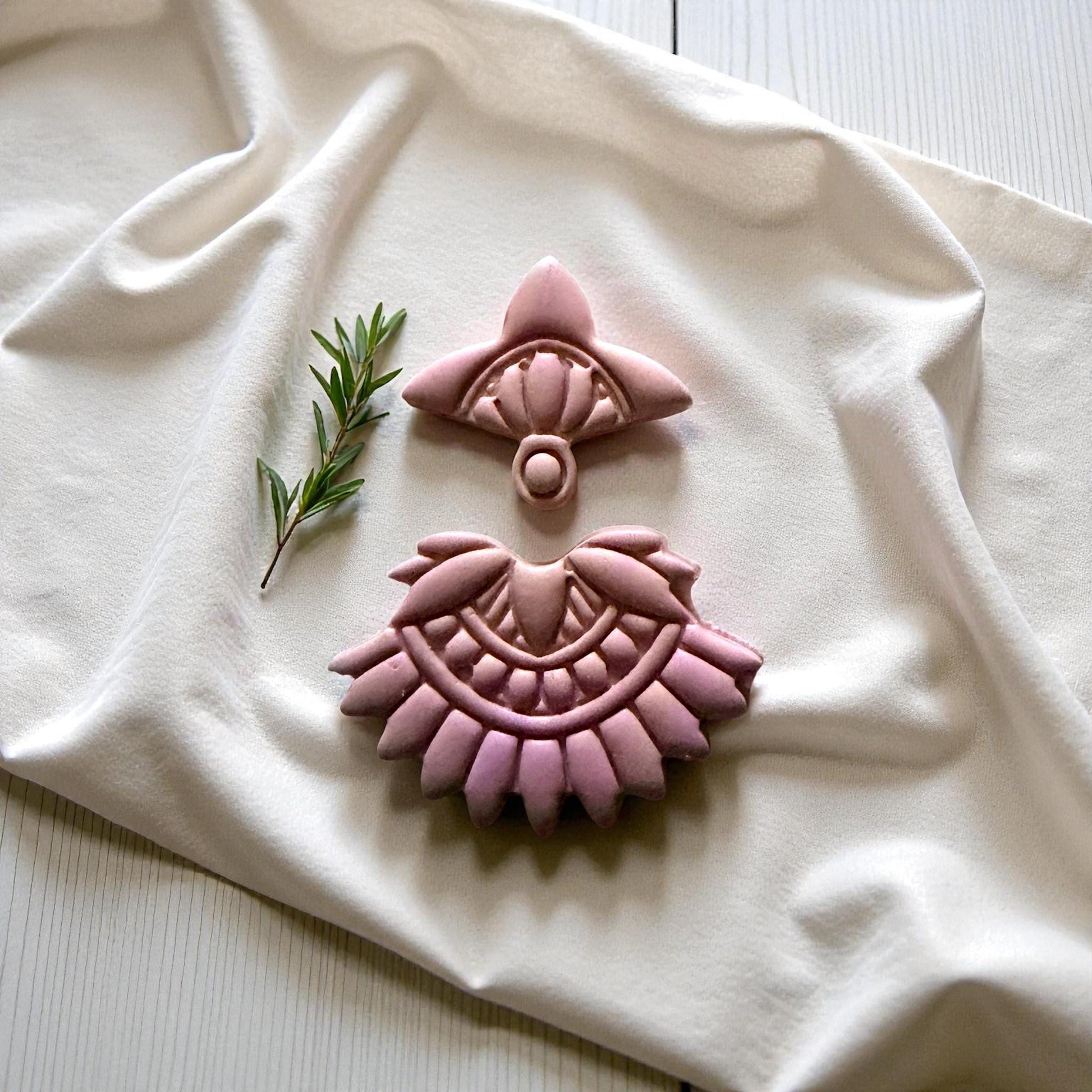 Close-up of pink clay boho fan pieces on ivory cloth with greenery