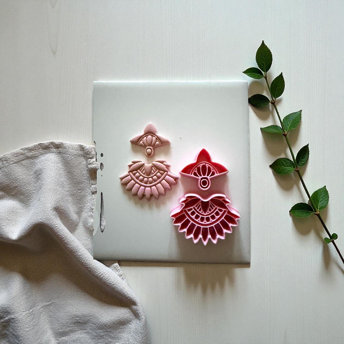 Pink and red boho fan clay imprints displayed with greenery on white tile
