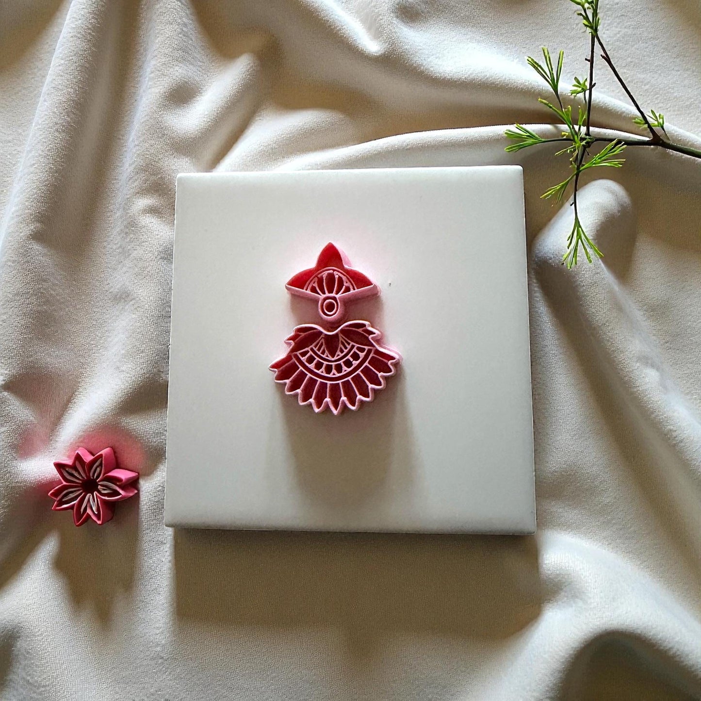 Red boho fan cutter on white tile with neutral cloth and small leaves