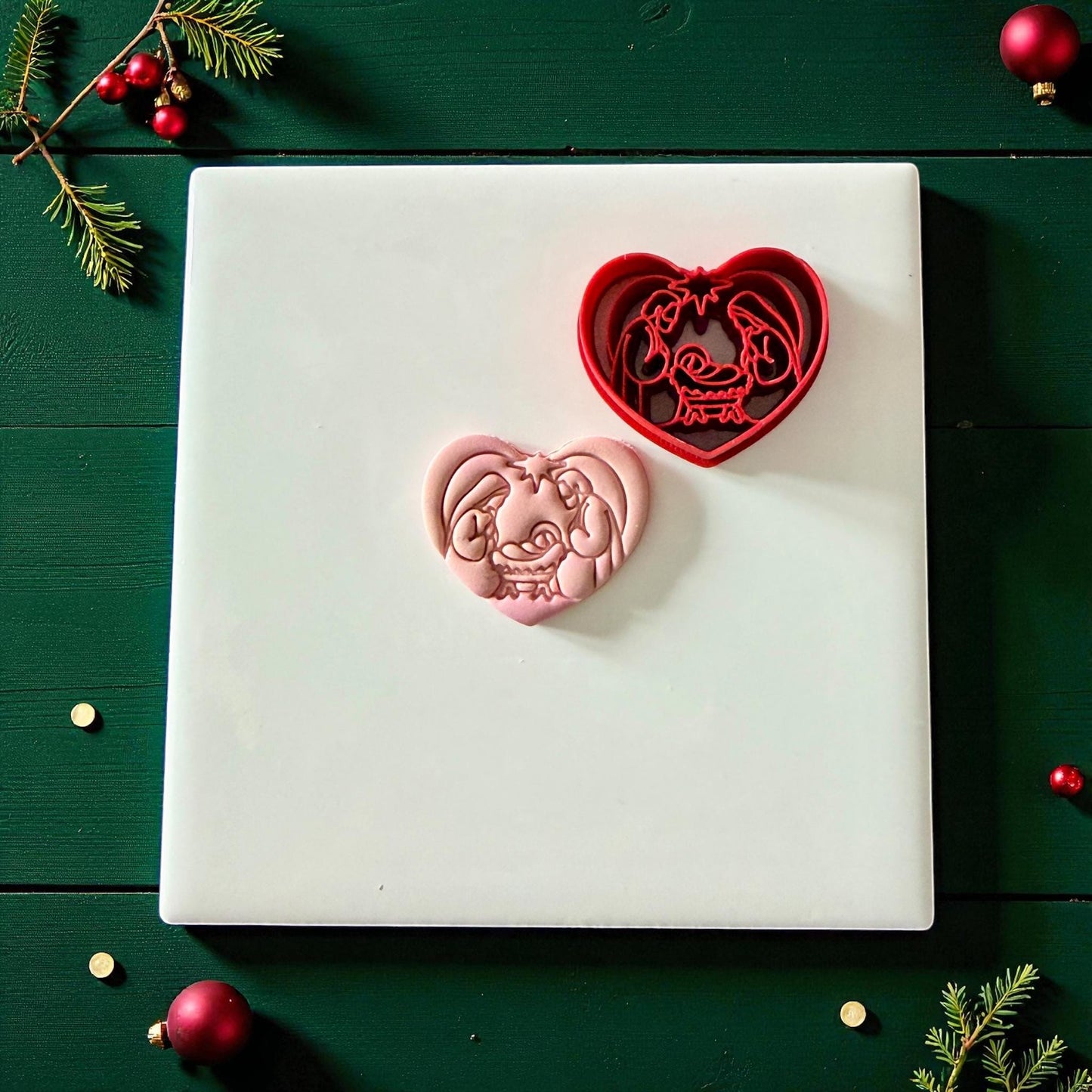 Heart nativity cutter and pink clay imprint on white tile surrounded by Christmas accents
