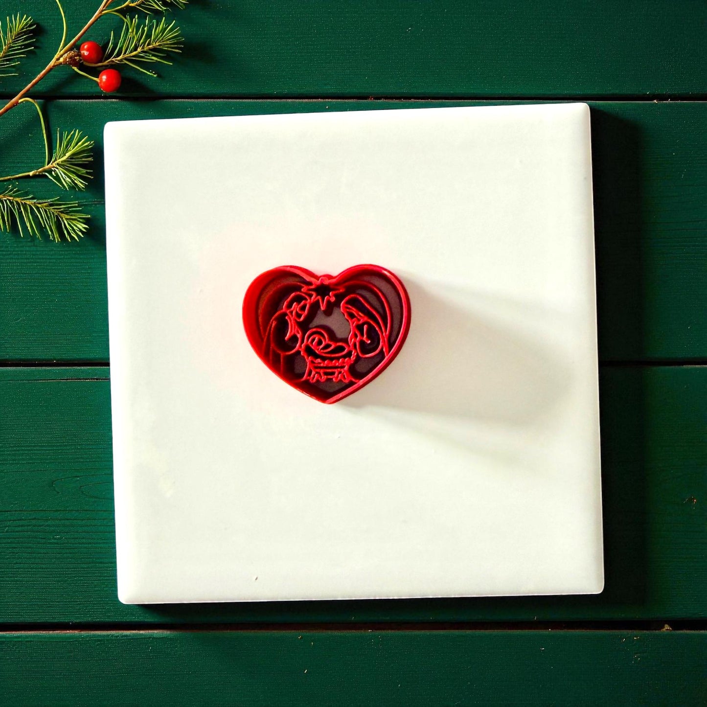 Heart nativity cutter centered on white tile with green wooden background and holiday decor