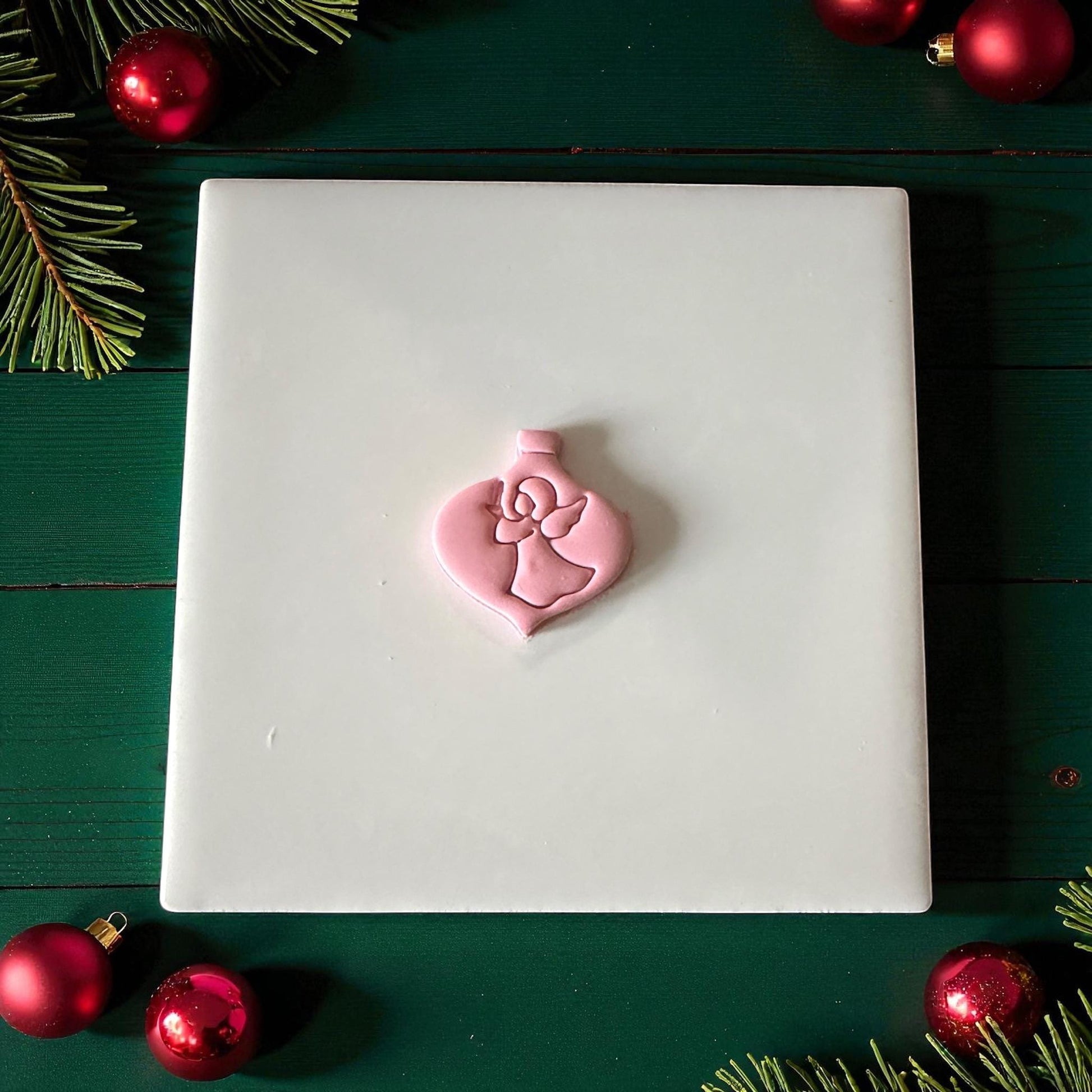Pink angel ornament clay imprint centered on white tile with green background