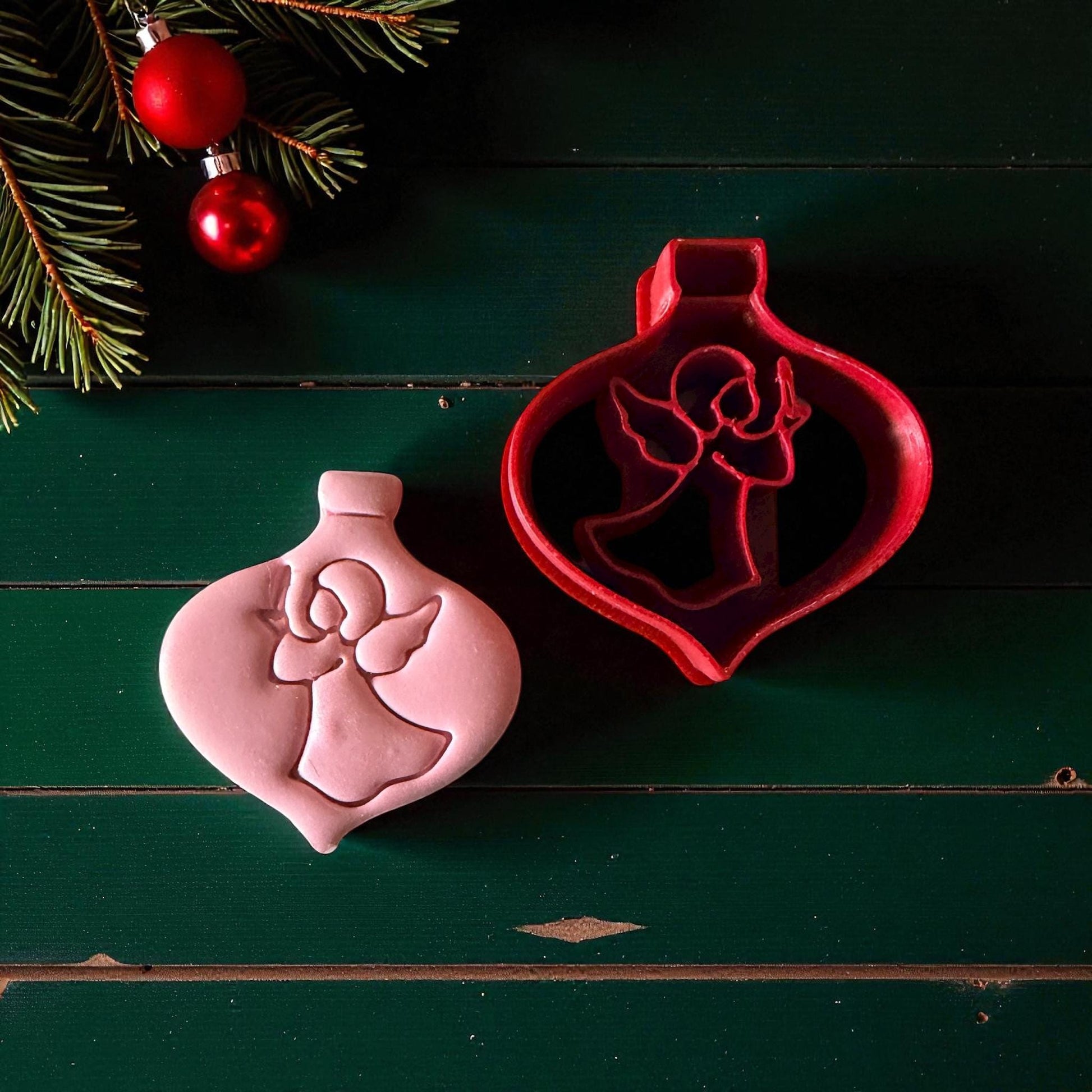 Angel ornament clay imprint and red cutter side by side with festive pine branches