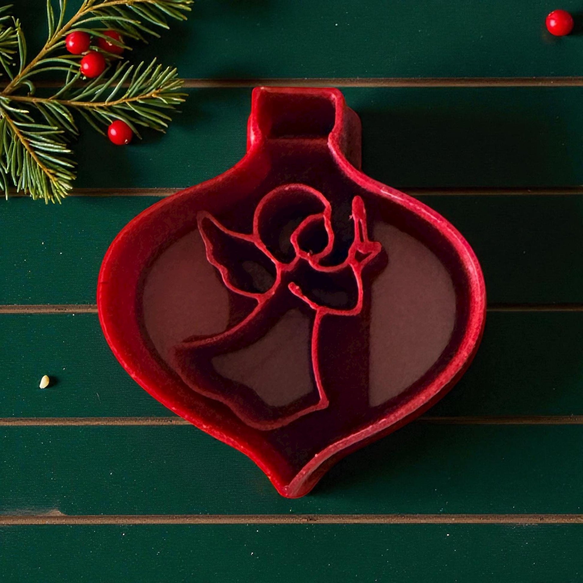 Red angel ornament polymer clay cutter on green wood with pine and red berries