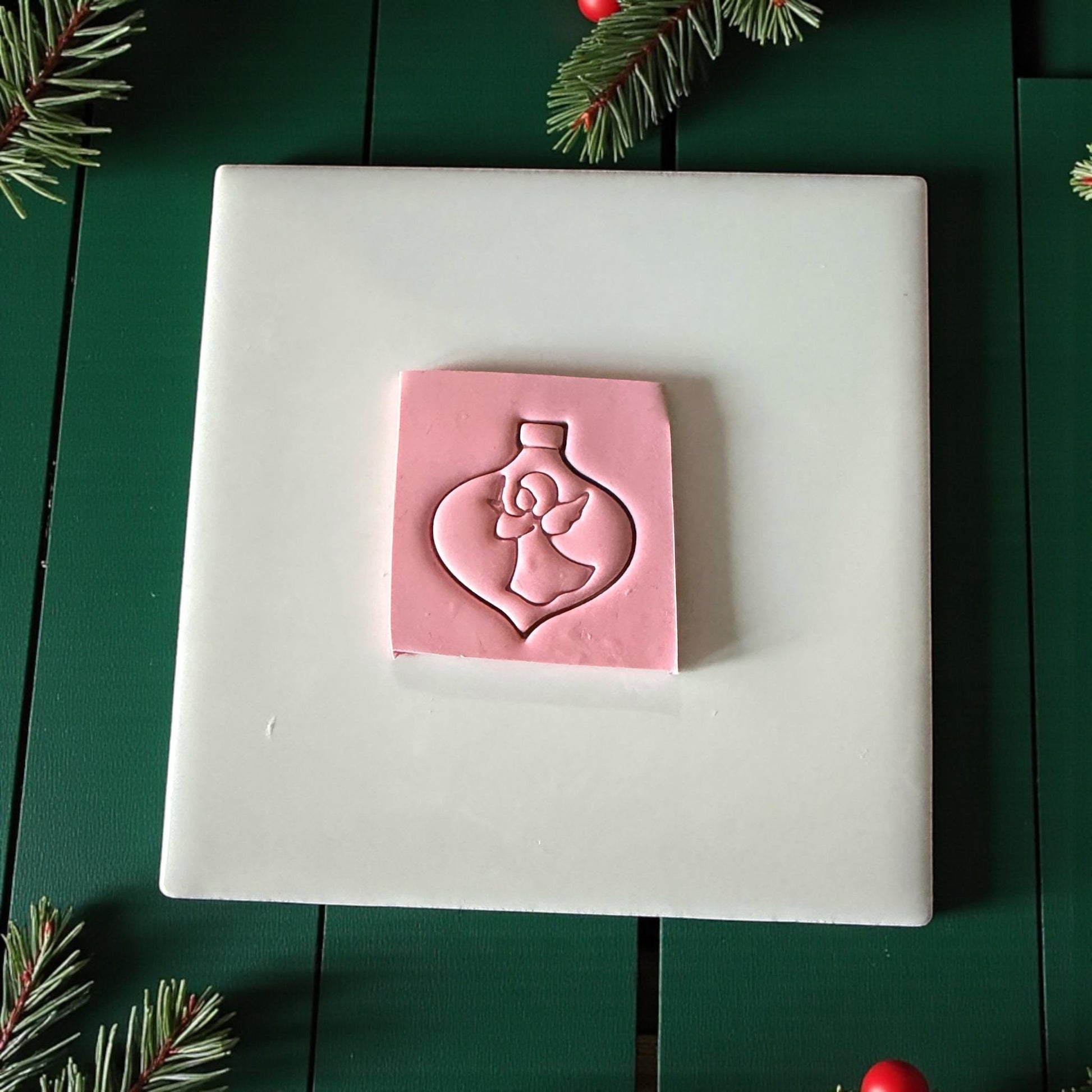 Angel ornament clay imprint on white tile surrounded by pine branches and red ornaments