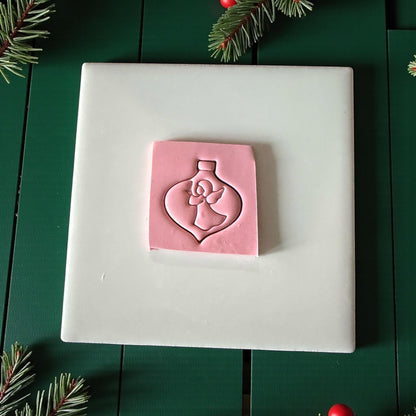 Angel ornament clay imprint on white tile surrounded by pine branches and red ornaments