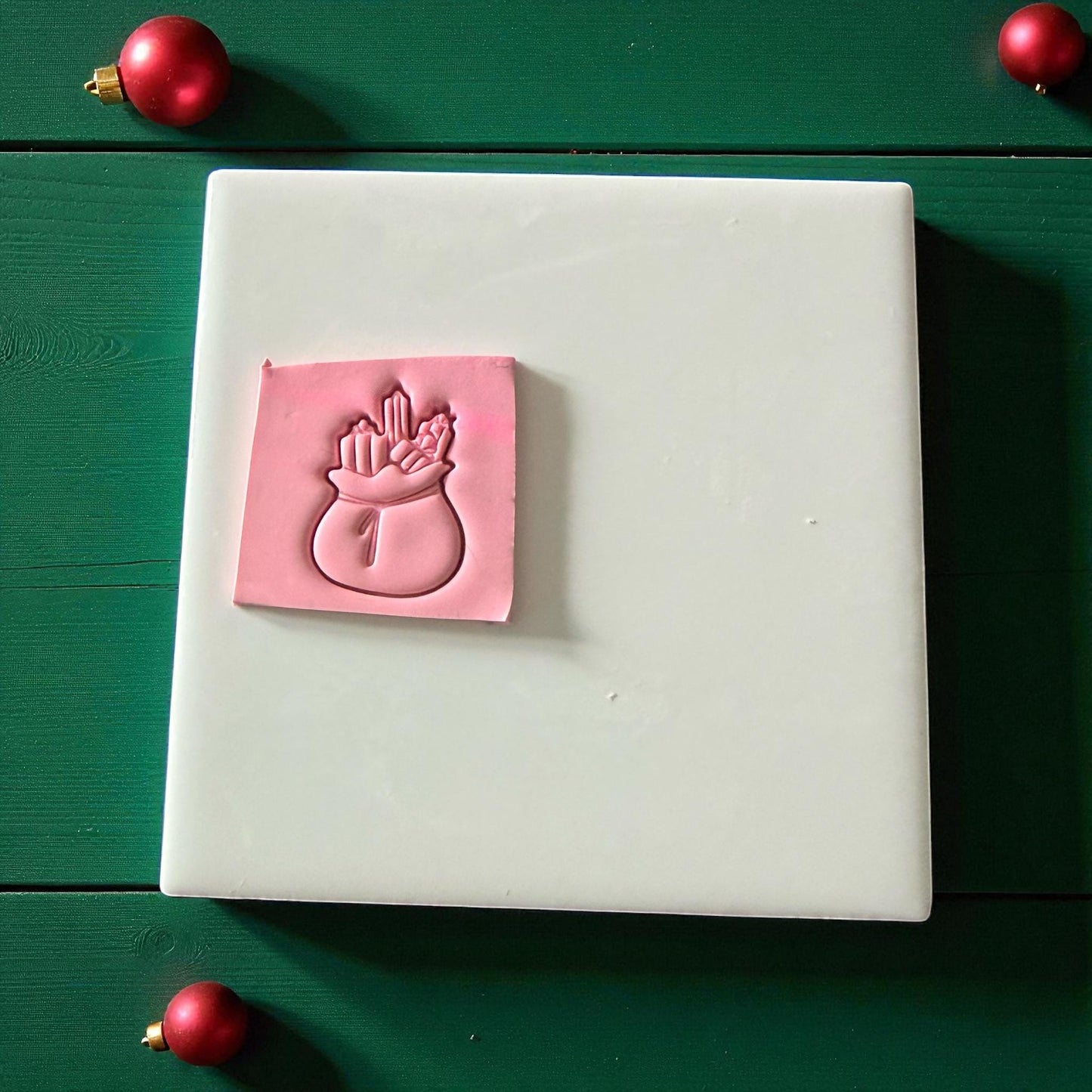 Pink Santa toy bag clay imprint on green wood background with red ornaments
