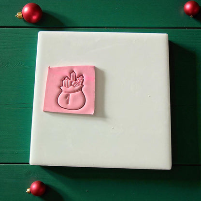 Pink Santa toy bag clay imprint on green wood background with red ornaments