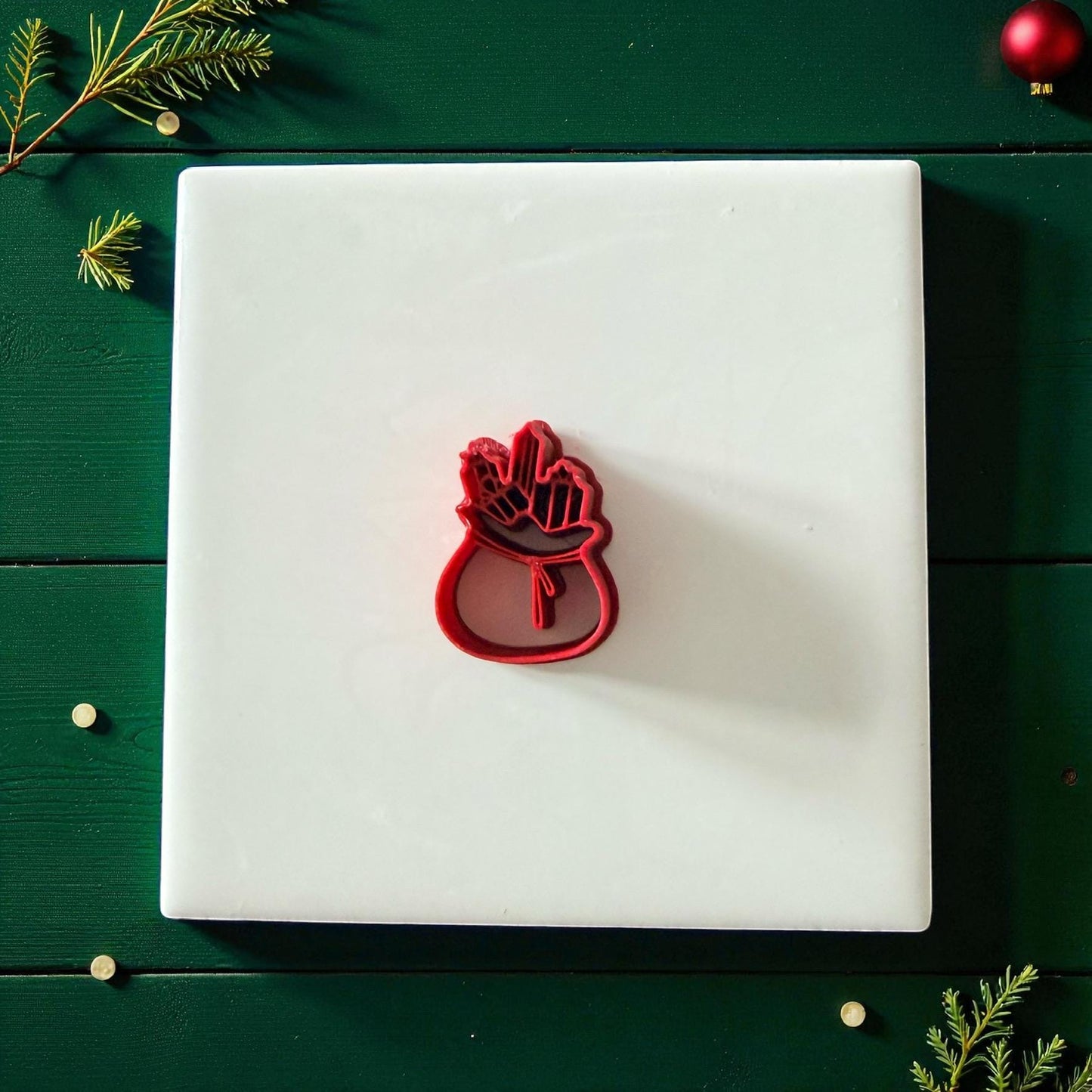 Red Santa bag of toys polymer clay cutter on green background with pine and ornament