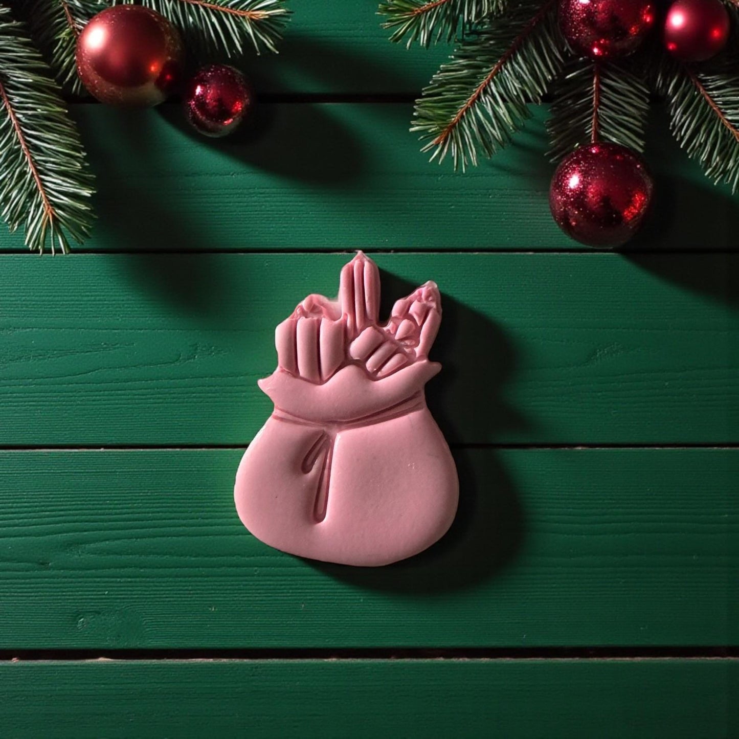 Pink Santa sack imprint centered on white tile surrounded by festive greenery