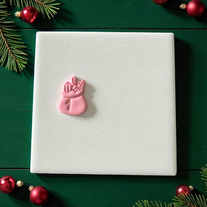 Pink Santa toy bag clay imprint on square piece of clay with red ornaments