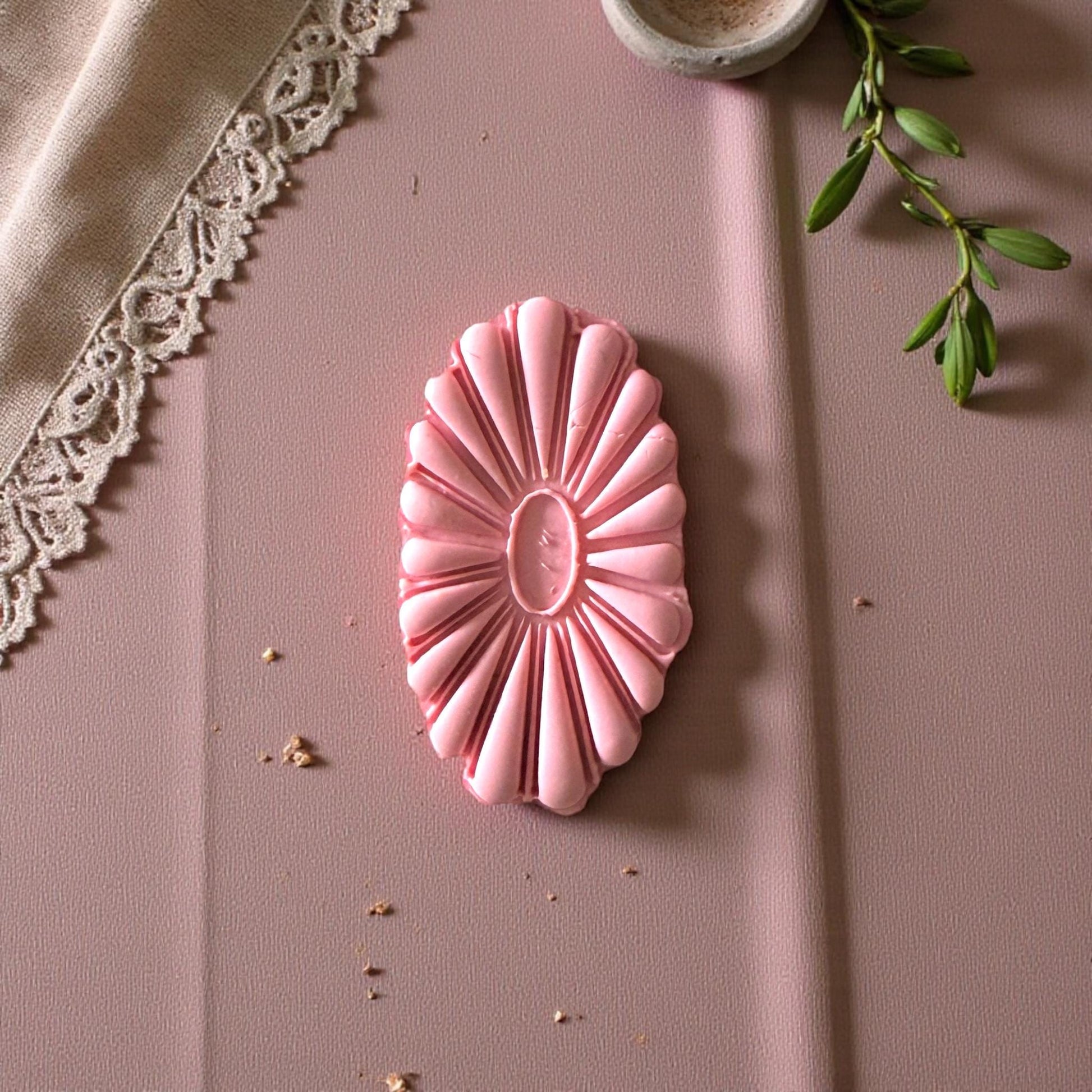 Oval flower cutter and matching clay imprint beside linen cloth and eucalyptus stem