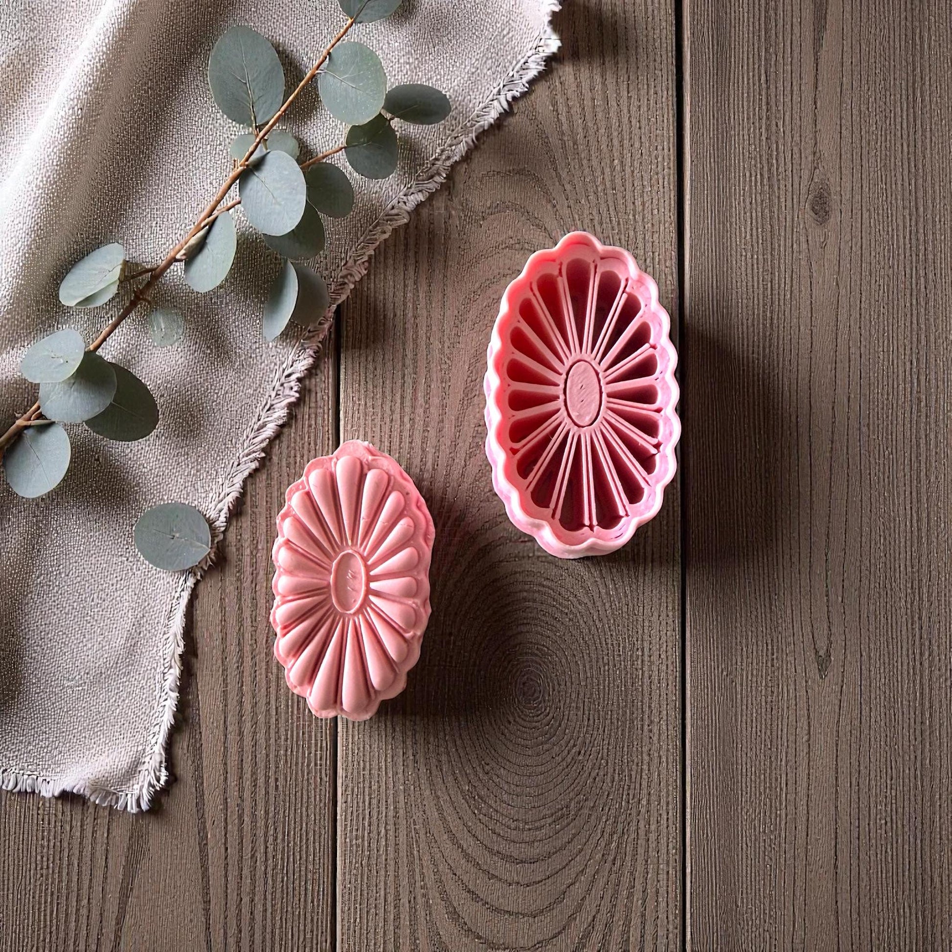 Two pink floral oval clay cutters and imprints on white tile with natural greenery