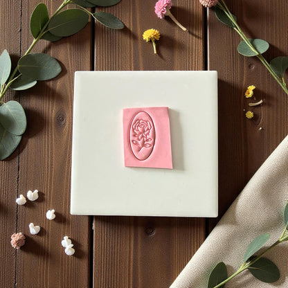 Pink rose cameo clay imprint on square piece of clay surrounded by eucalyptus and dried flowers