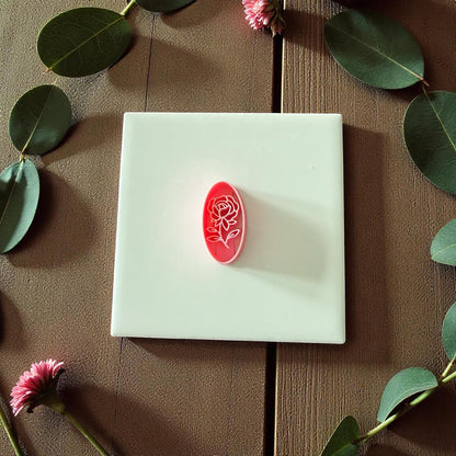 Oval rose floral clay cutter centered on white tile with eucalyptus leaves and pink flowers