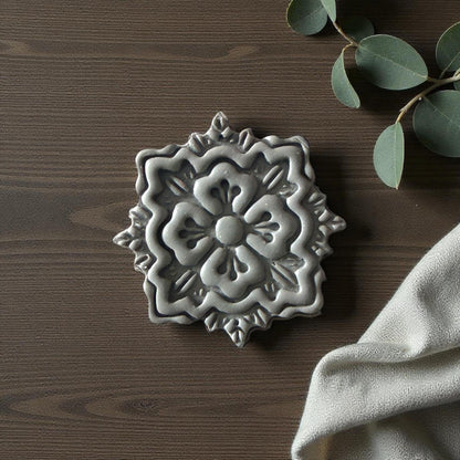 Gray floral medallion clay imprint on wood background with eucalyptus and beige fabric