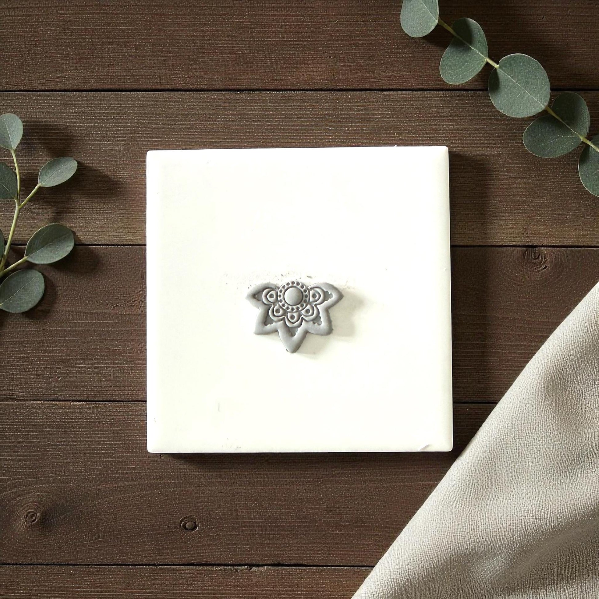 Gray lotus clay imprint on white tile with eucalyptus
