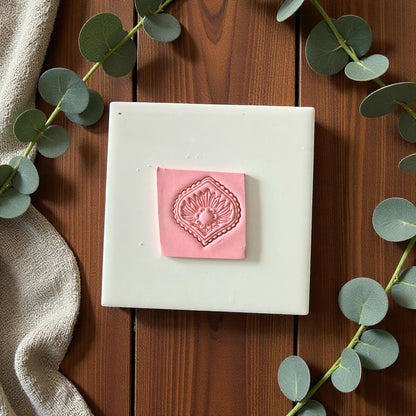 Pink diamond clay imprint on square piece of clay surrounded by eucalyptus leaves