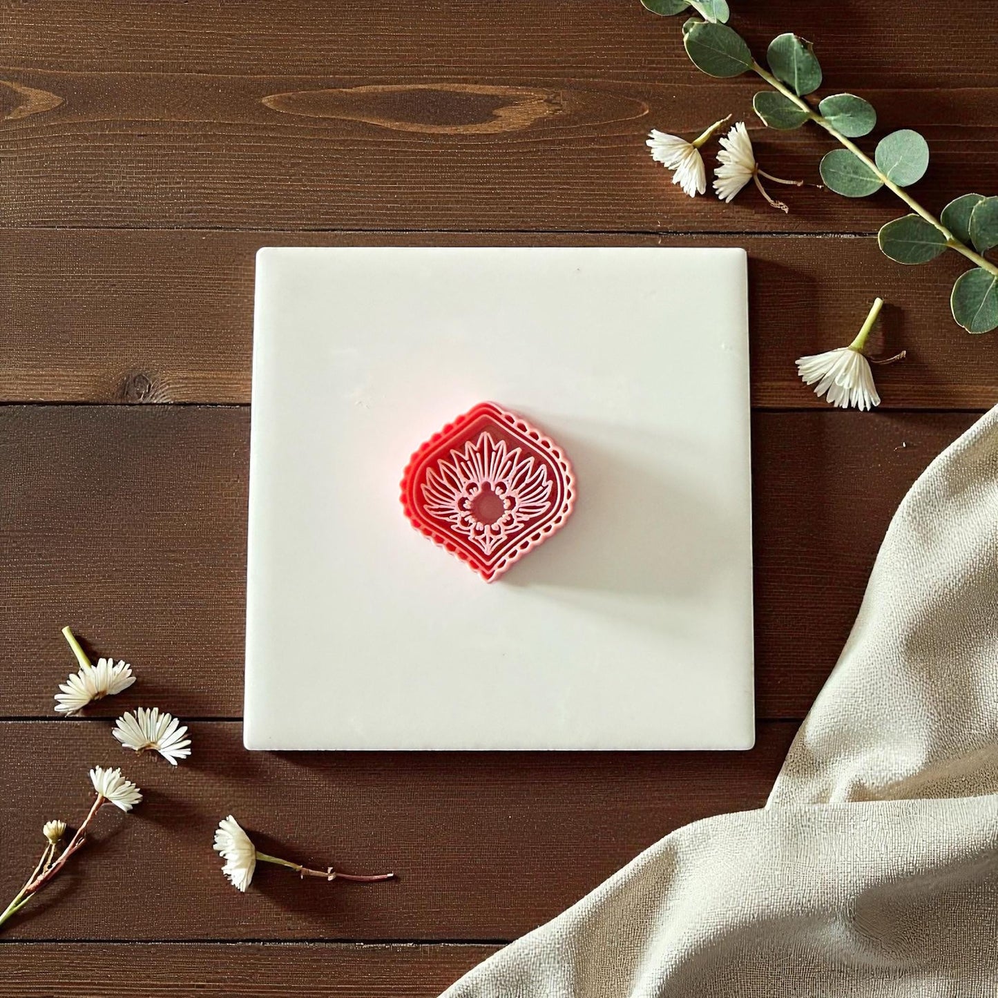 Pink diamond sunburst clay cutter beside imprint on white tile surrounded by greenery