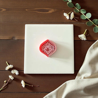 Pink diamond sunburst clay cutter beside imprint on white tile surrounded by greenery