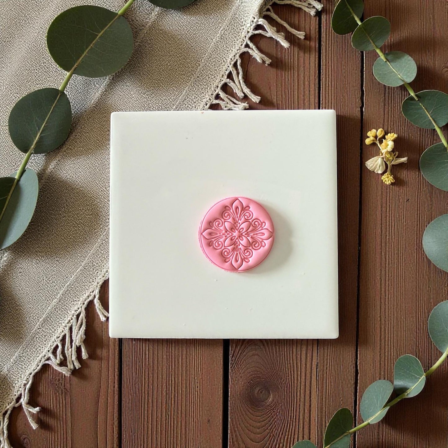 Small floral medallion clay imprint on white tile framed with eucalyptus branches