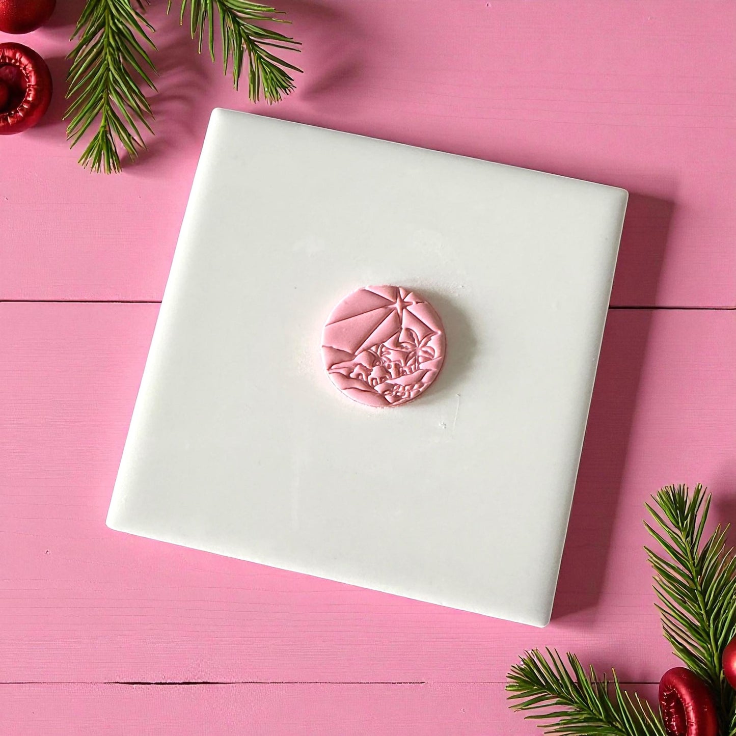 Round Bethlehem town clay imprint on pink background with Christmas greenery