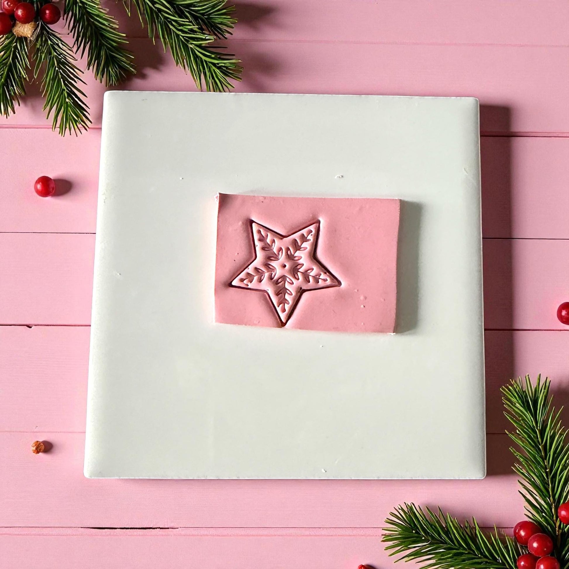 Pink Nordic star clay imprint on white tile with pine branches and berries