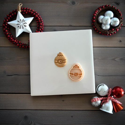 Two Santa belt ornament clay imprints side by side on white tile with ornaments