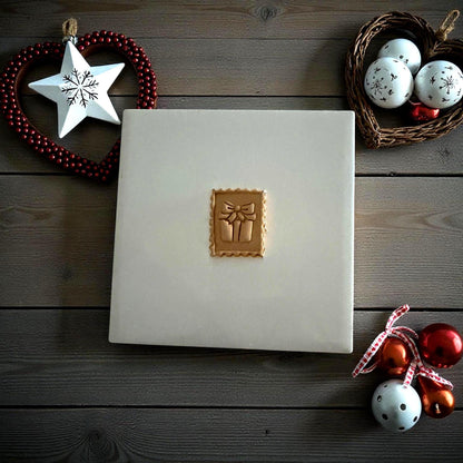 Gift stamp clay imprint centered on white tile surrounded by holiday ornaments