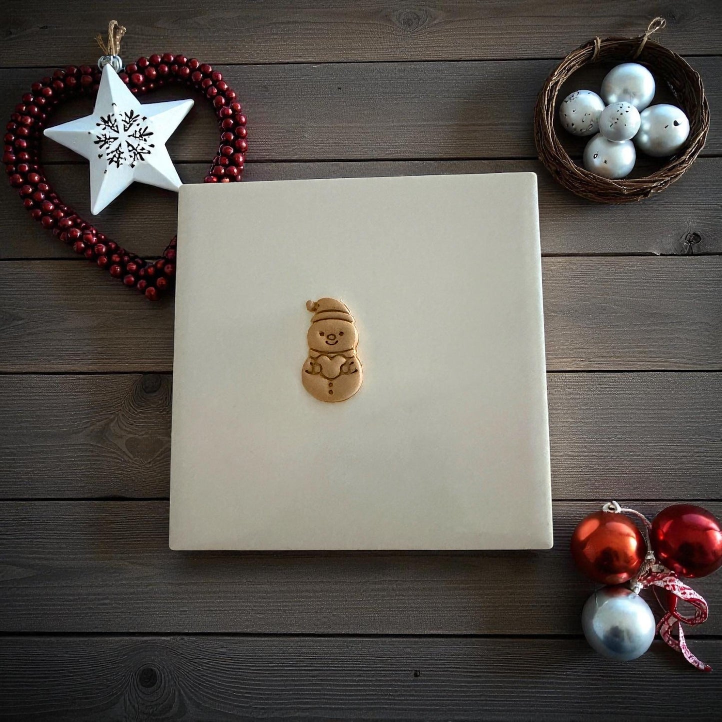 Small snowman clay imprint centered on white tile with holiday ornaments