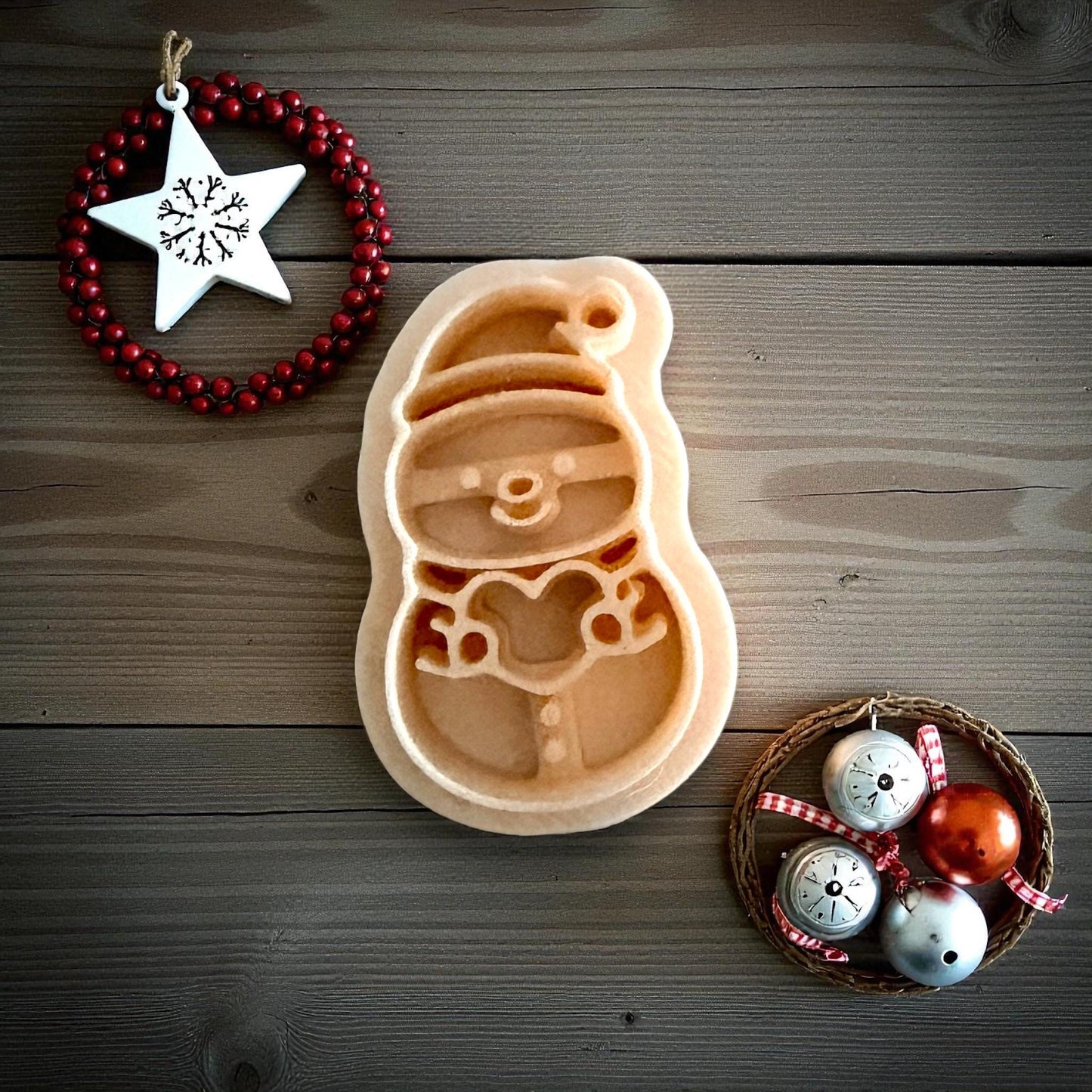 Snowman holding heart clay imprint on tan sheet with ornaments on white tile