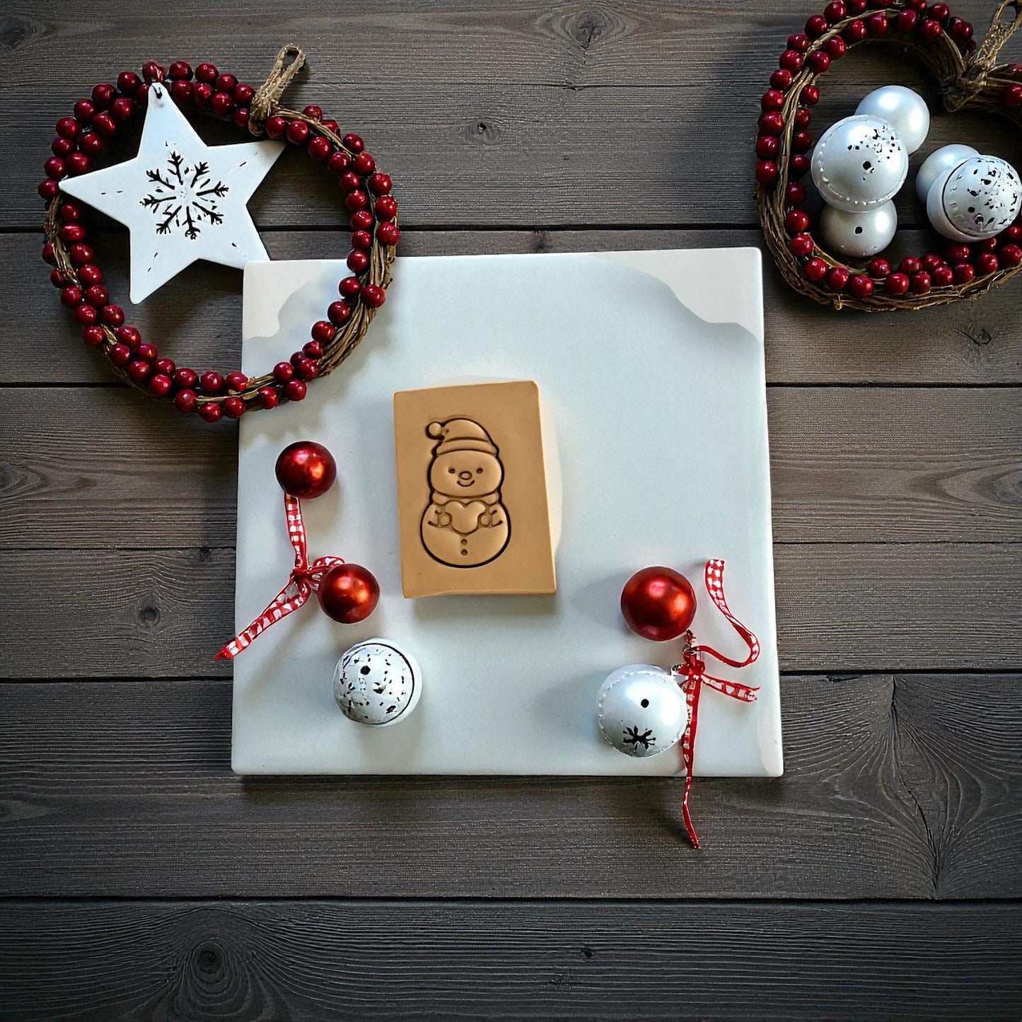 Snowman holding a heart clay imprint on wood background with Christmas decor