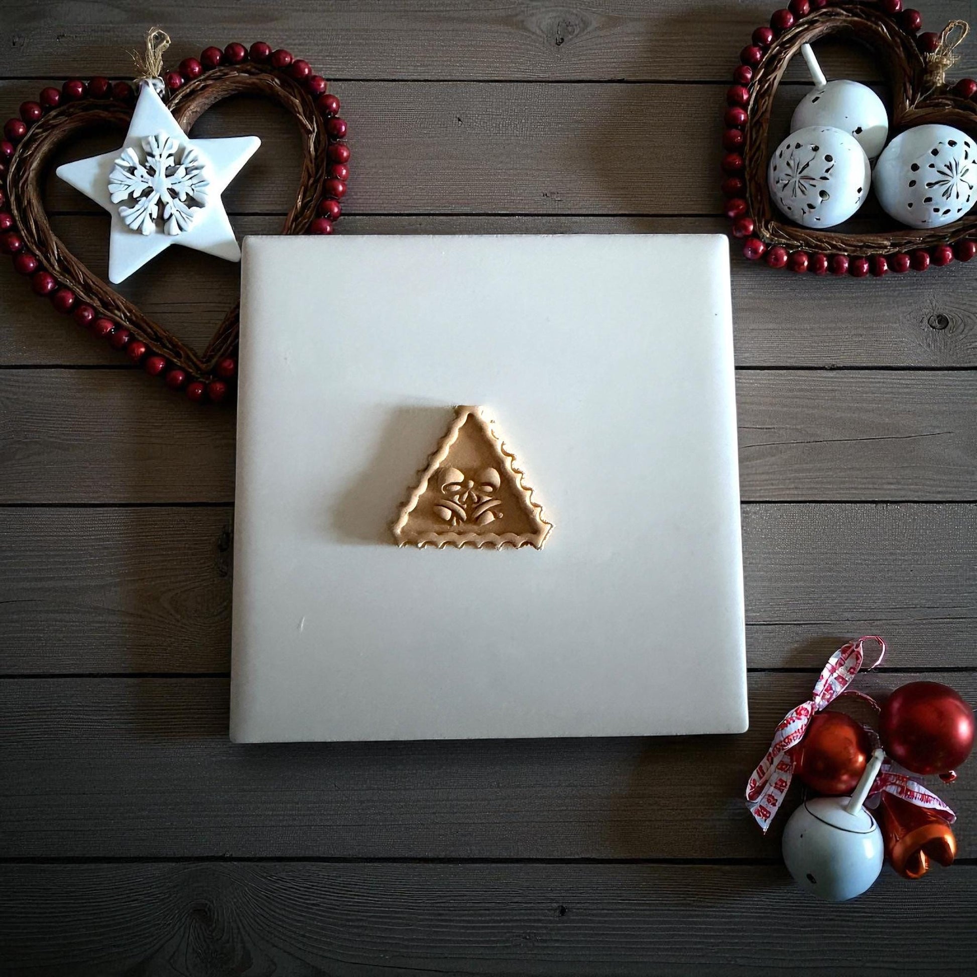 Small jingle bell clay imprint centered on white tile surrounded by Christmas decor
