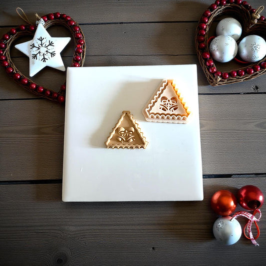 Two triangle jingle bell clay imprints side by side on white tile with festive ornaments