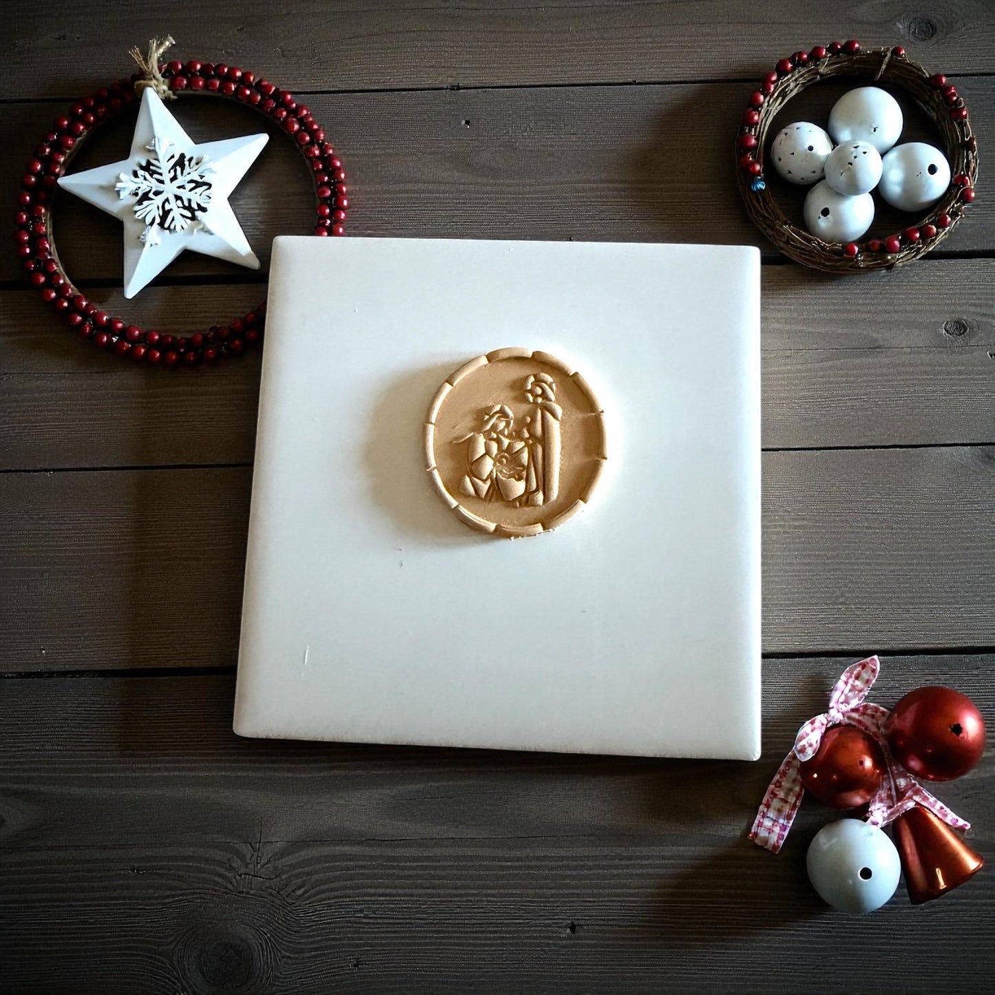Small nativity clay imprint centered on white tile with Christmas decorations