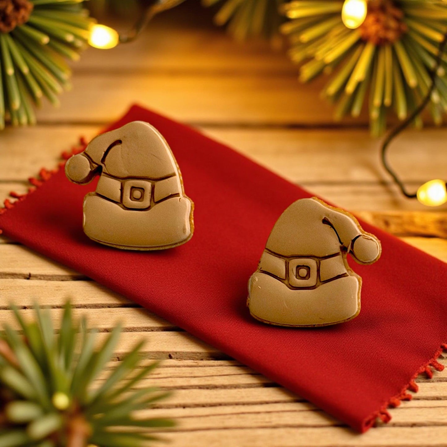 Two tan Santa hat clay imprints on red napkin with Christmas lights in background