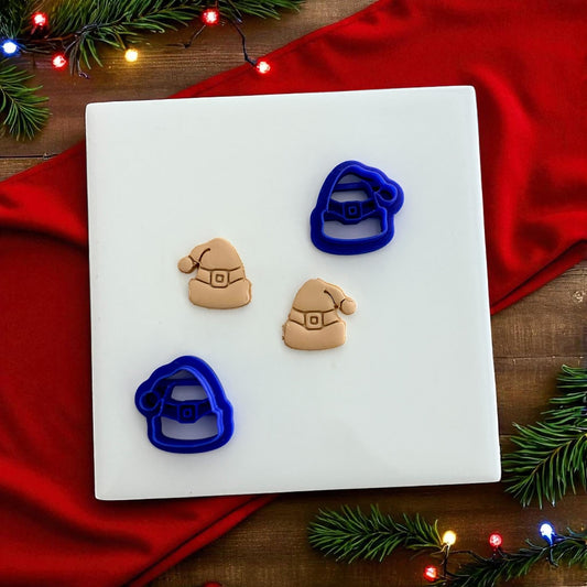 Blue Santa hat clay cutters with tan clay imprints on wooden surface and string lights
