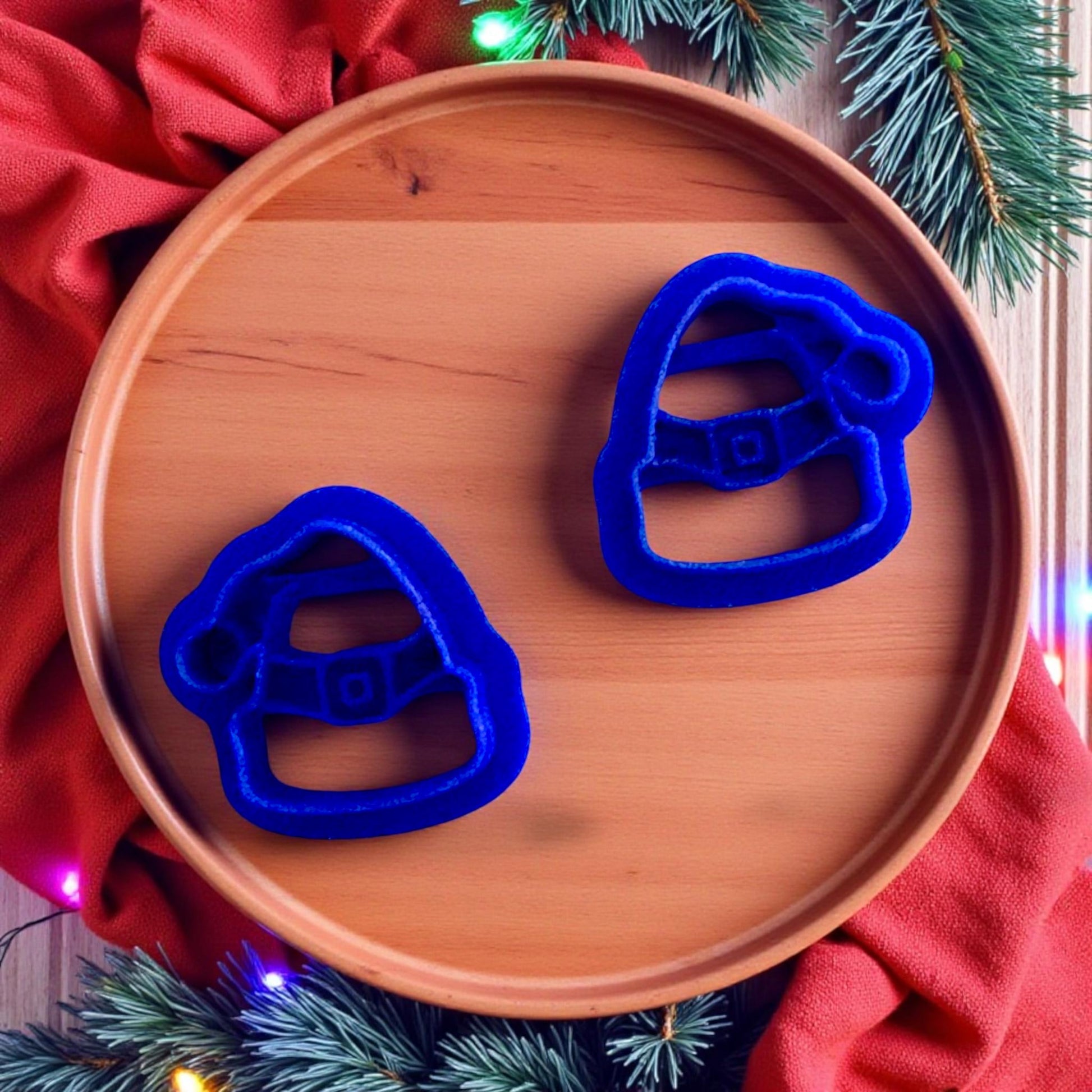 Close up of Blue Santa hat polymer clay cutters on wooden plate with red fabric and pine branches
