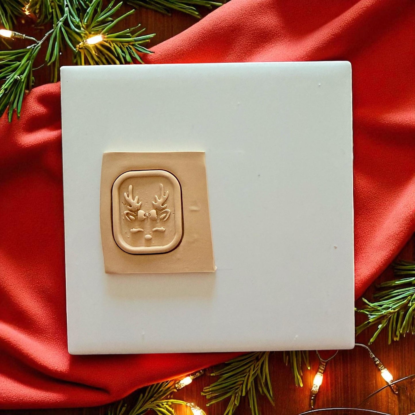 Clay slab with reindeer face cutter impression surrounded by red fabric and lights