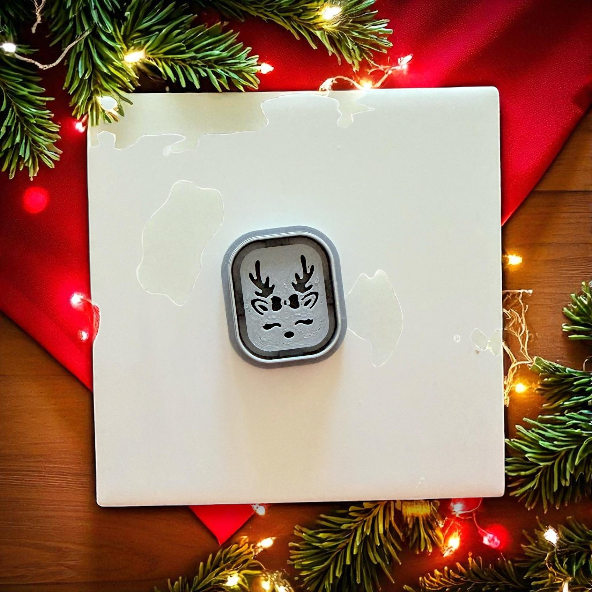 Small reindeer clay cutter centered on white tile with red fabric and holiday lights