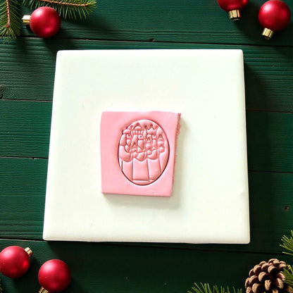 Pink Three Kings clay imprint on white tile surrounded by pine and red ornaments