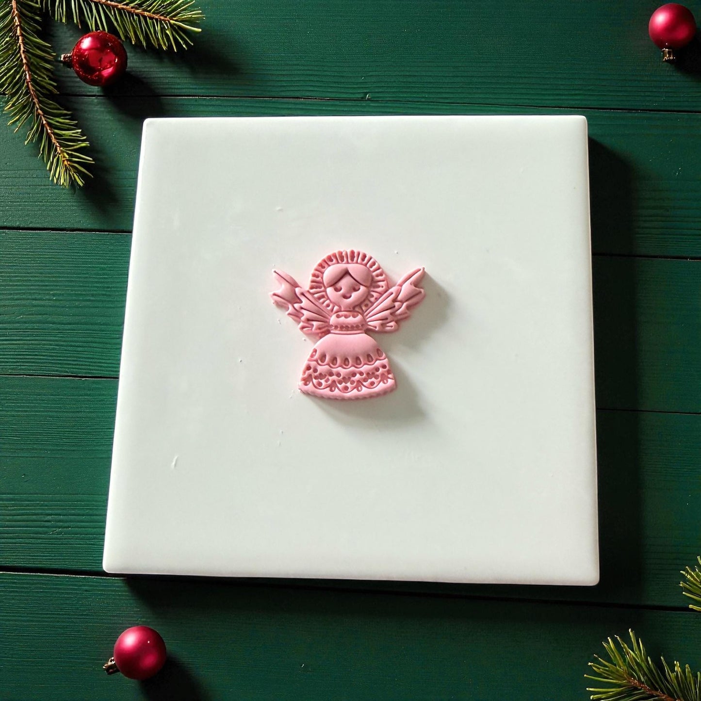 Small pink angel clay imprint centered on white tile with evergreen branches