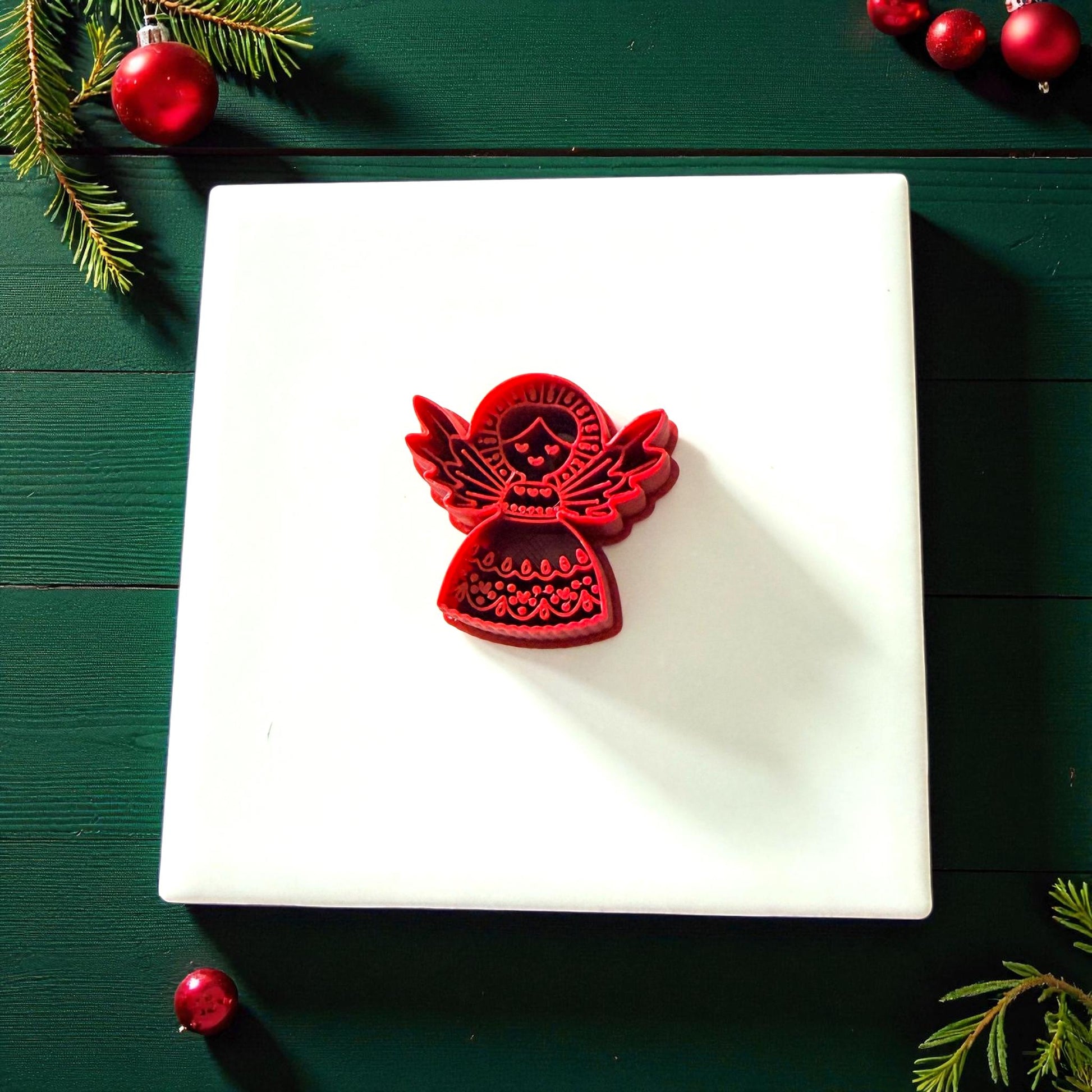 Red folk angel cutter centered on white tile with holiday ornaments