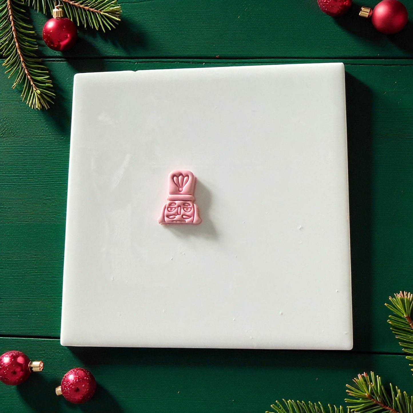 Pink nutcracker clay imprint centered on white tile with red ornaments