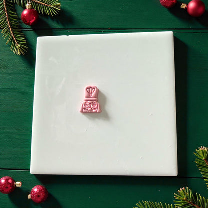 Pink nutcracker clay imprint centered on white tile with red ornaments