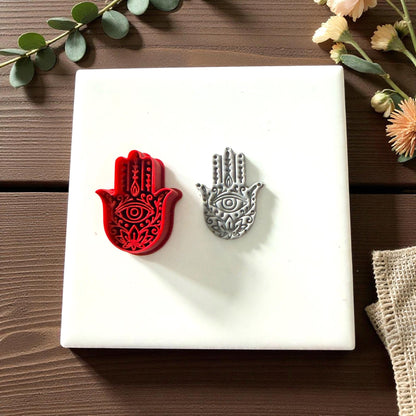 Red Hamsa clay cutter beside gray clay imprint on white tile