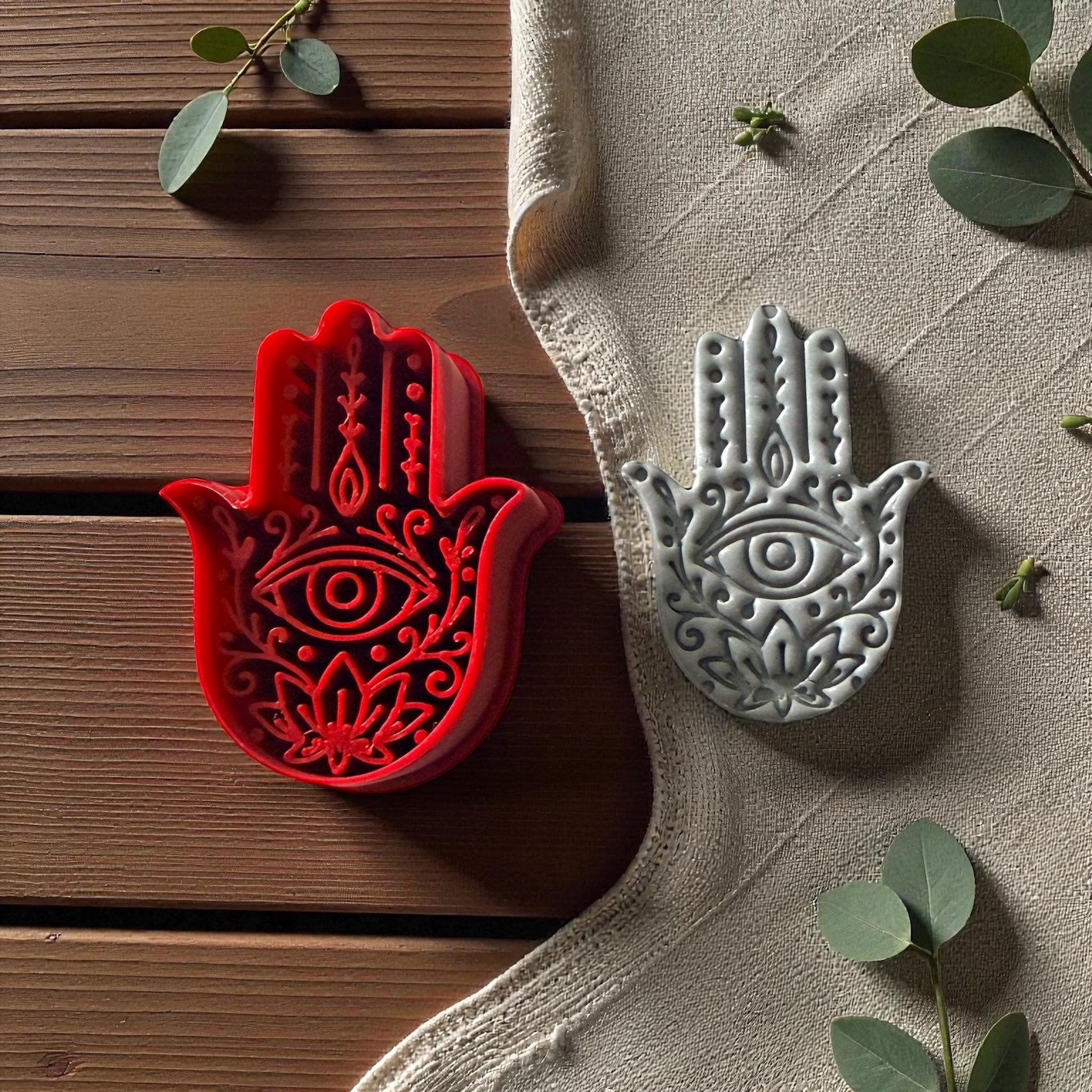 Red Hamsa cutter and gray clay imprint on beige fabric with green leaves