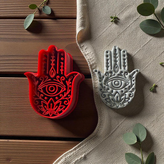 Red Hamsa cutter and gray clay imprint on beige fabric with green leaves